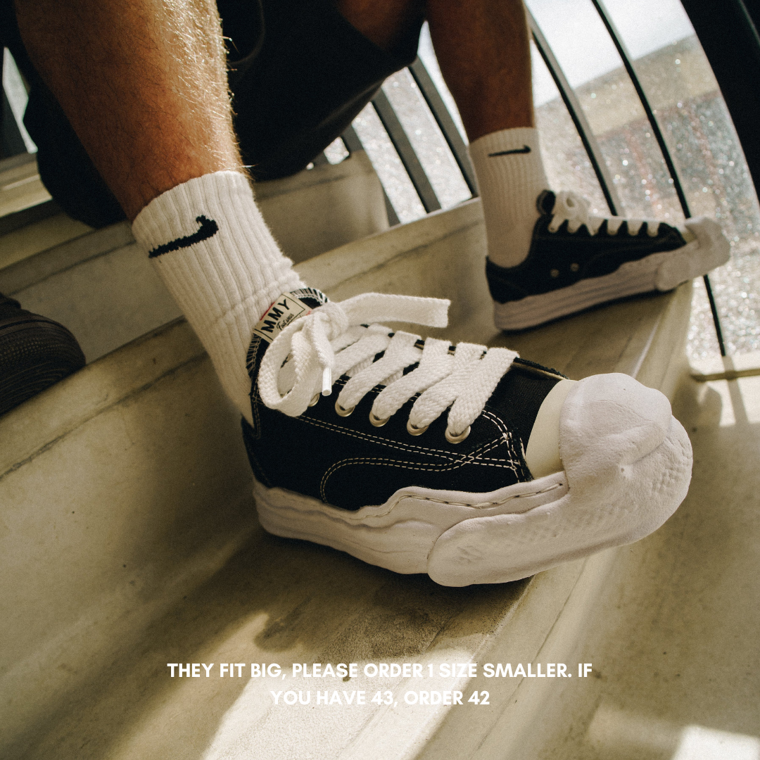 Close-up of person wearing Maison Mihara Yasuhiro Hank OG Sole Canvas Low Black sneakers paired with white Nike socks, showcasing exclusive Europe sneaker style with thick white laces and distinctive sole design. The real deal.